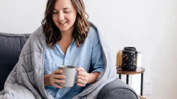 Official Velin photo of an adult seated on a sofa under a grey weighted blanket